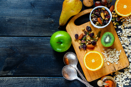Close up of dark rustic table with healthy breakfast. Oat flakes with pumpkin seeds, honey, nuts, dry berries and fresh fruits on vintage wooden background. Top view. Copy-space.の写真素材