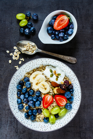 Healthy food background with plate of oat flakes, berries with yogurt and seeds for tasty breakfast on dark vintage boardの写真素材