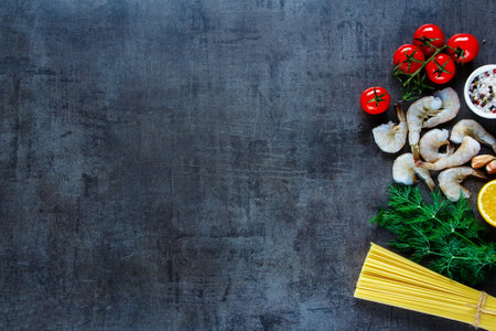 Top view of ingredients for pasta with seafood. Shrimps, spaghetti, dill, garlic, spices and cherry-tomatoes on dark grunge backdrop, place for text, border.の写真素材