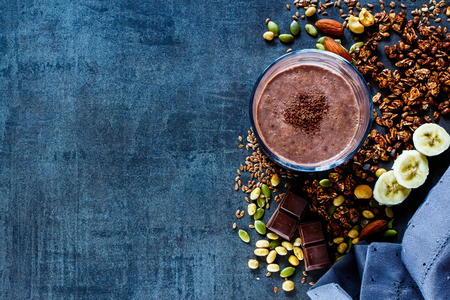 Top view of fresh banana chocolate smoothie with homemade granola, nuts and seeds on dark vintage background with space for text, banner. Healthy ingredients set.の写真素材
