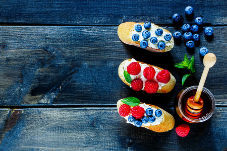 Top view of dessert sandwiches with fresh berries blueberry and raspberry, cream cheese, mint and honey over old dark wooden textured background with space for text.の写真素材