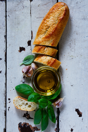 Old white wooden table with baguette cut in slices, fresh basil, spices and olive oil over rustic backdrop, top view.の写真素材