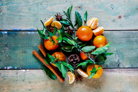 Old wooden table with tangerines green leaves, pine cone and cinnamon sticks over rustic background. Top viewの写真素材