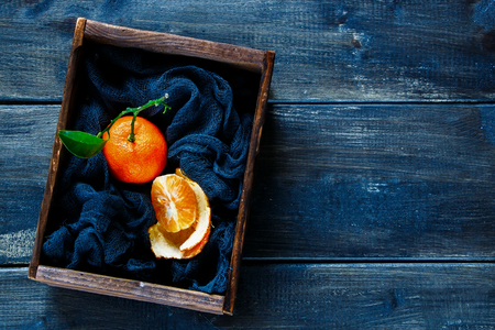 Vintage box of juicy ripe tangerine with leaves and slices at textile napkin on rustic wooden backdrop, top view, copy space. Orange mandarin over wood.の写真素材