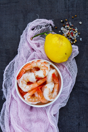 Top view of fresh pink shrimps on plate, lemon and spices over vintage stone backdrop. Preparing seafood background.の写真素材