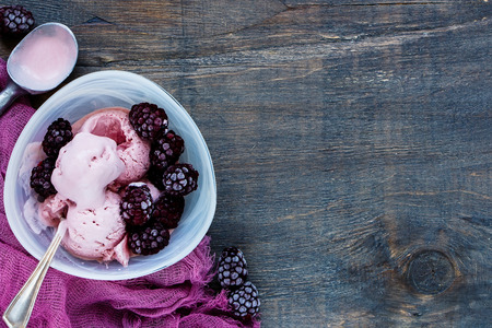 Ceramic bowl of melting blackberry ice-cream with frozen berries over dark wooden background, top view, copy space, horizontal composition. Homemade Organic productの写真素材