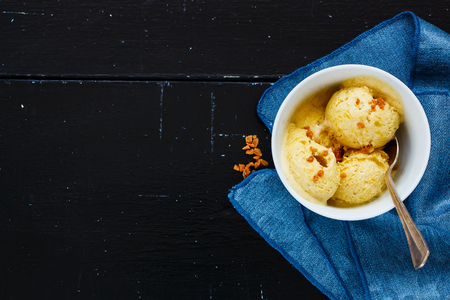 Close up of homemade fruit ice cream scoops with caramel pieces in white bowl on old black backdrop, copy space, top view.の写真素材