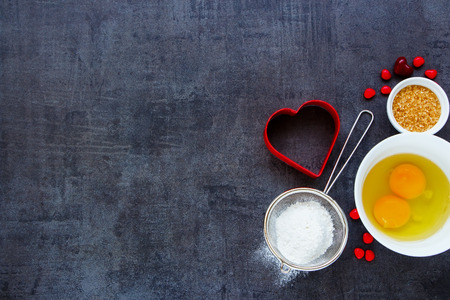 Baking ingredients background with raw eggs, brown sugar, flour and red heart shape cookie cutter on vintage backdrop, top view, copy space.の写真素材