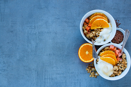 Close up of diet breakfast yogurt bowls with baked granola, orange, dried fruit, nuts and seeds over grey  background, top view. Clean eating, vegetarian, vegan or dieting conceptの写真素材
