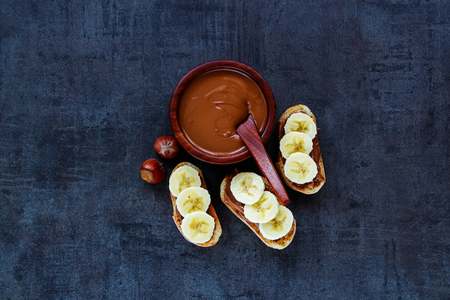 Top view of delicious sweet hazelnut and chocolate spread sandwiches with sliced bananas for breakfast on vintage slate background.の写真素材