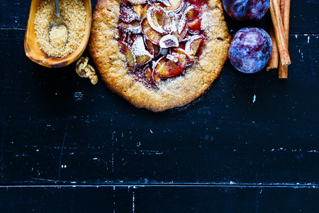 Freshly made wholegrain plum pie or tart with walnuts and fresh plums on vintage wooden background. Top view. With copy space. Flat lay styleの写真素材