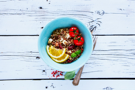 Top view of salad with quionoa, beans, fresh tomatoes, basil, feta cheese and green olives in bowl on white grunge wooden background. Weight loss food concept. Flat layの写真素材