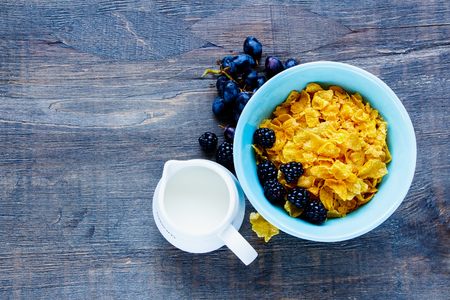 Breakfast theme table with bowl of corn flakes, milk, grapes and fresh blackberries on vintage wooden background. Top view. With copy space. Flat lay styleの写真素材