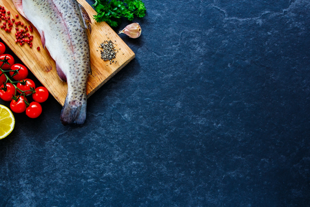 Delicious fresh seafood. Fish with ingredients - healthy food, diet or cooking concept. Whole raw fish on dark vintage texture. Food background, top view, flat lay style.の写真素材