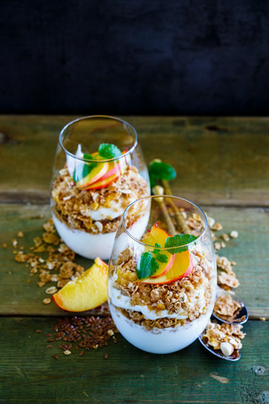 Close up of detox breakfast. Greek yogurt, granola, peach layered parfait in glasses with mint leaves over wooden background, copy space, selective focus. Clean eating, detox, dieting food conceptの写真素材
