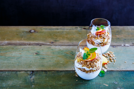 Homemade detox breakfast. Greek yogurt, granola, peach layered parfait in glasses with mint leaves over wooden background, copy space, selective focus. Clean eating, detox, dieting food conceptの写真素材