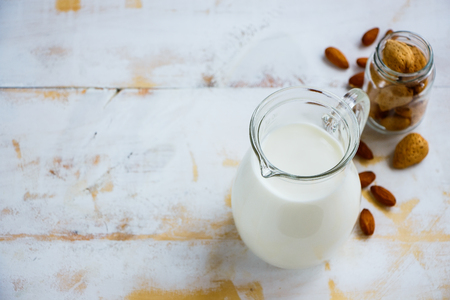 Vegetable sources of protein. Close up of almond milk in jug and nuts over old white wooden background, selective focus, copy space. Clean eating, dairy-free, vegan, detox, allergy-friendly, healthy food conceptの写真素材
