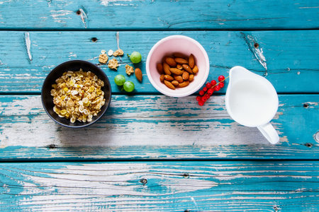 Flatlay of healthy breakfast preparation with ingredients: muesli, nuts, milk and berries on...