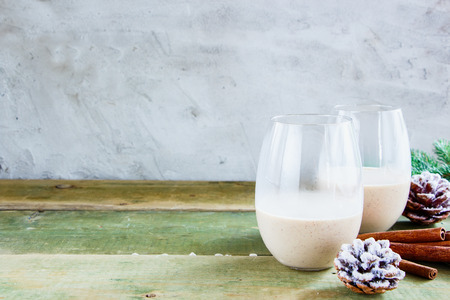 Traditional winter eggnog in glasses with milk, rum and cinnamon, christmas decorations on wooden table. Concrete background, selective focusの写真素材