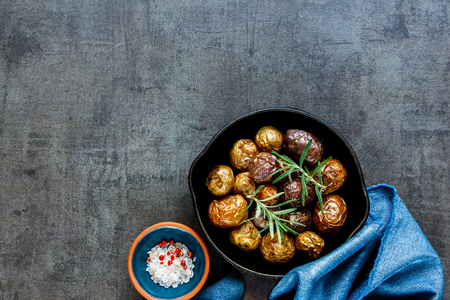 Homemade fried baby potatoes in vintage cast iron pan on black concrete background, copy space. Healthy food concept. Overhead shotの写真素材