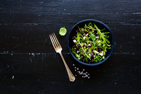 Healthy beetroot, arugula, feta cheese and pumpkin seed salad in black ceramic plate over rustic wood background, top view. Flat lay composition with copy space.