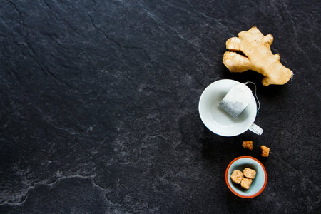 Flat-lay of tea composition on dark concrete background: tea, brown sugar, ginger.