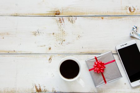 Flat lay office workplace with phone, headphones, gift and coffee on white wooden background, top view. Free space for textの写真素材