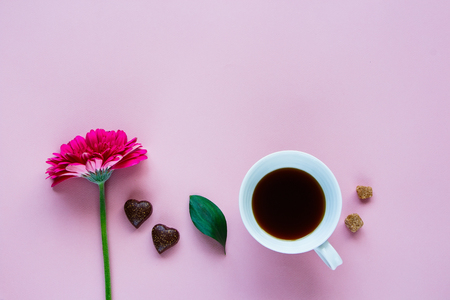 Coffee mug, beautiful pink gerbera flower and chocolate on pink background. Greeting card for Birthday, Woman or Mothers Day. Top view, flat layの写真素材