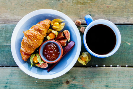 Continental breakfast plate with freshly baked croissant, apricot jam, ripe fruit and coffee cup on old wooden table, top view. Healthy breakfast conceptの写真素材