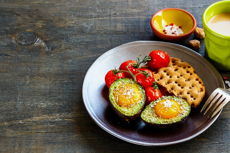 Close up of cracker, tomatoes and avocado baked with eggs on plate over dark wooden background, side view. Clean eating food concept. Healthy vegetarian breakfast conceptの写真素材