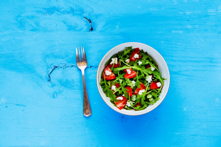 Flat lay of strawberry arugula feta cheese salad bowl served on blue painted wood copy space background. Top viewの写真素材