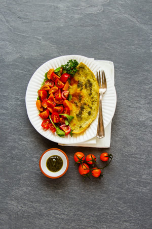 Healthy breakfast or diet lunch flat-lay. Omelette with pesto sauce, arugula and tomatoes salad on...
