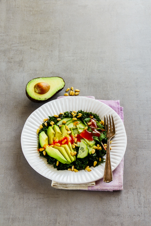 White plate of green vegan salad with kale, avocado, cucumber, pine nuts and honey dressing on light concrete background selective focus. Clean eating, slimming, diet, vegan food concept.の写真素材