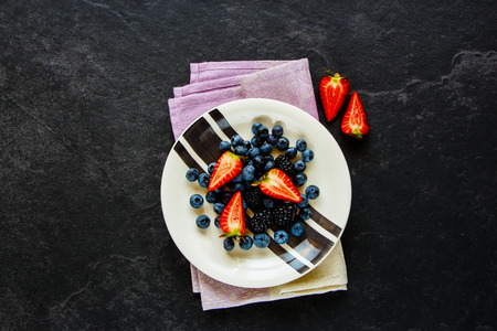 Organic berry plate flat-lay. Fresh strawberry, blueberry and blackberry. Mix of summer berries on stone background, superfood and detox concept. Top viewの写真素材