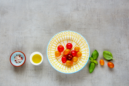 Ingredients for tomato salad flat lay. Colorful tomatoes in bowl, basil and olive oil on light background with copyspace. Top viewの写真素材