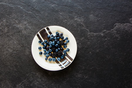 Fresh blueberry and blackberry on stone background, plate of organic black berry, superfood and detox concept. Flat lay style, top viewの写真素材