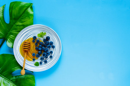Wild blueberry and honey in plate on pastel blue background flat lay