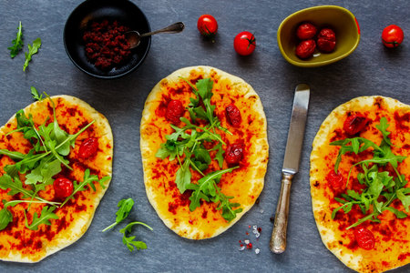 Flat-lay of freshly baked vegetarian pizza with vegetables and sun-dried tomato pesto