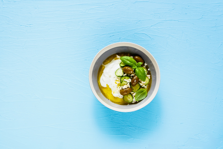 Greek yogurt with olives, feta cheese, cucumber, olive oil and basil on blue background flat layの写真素材