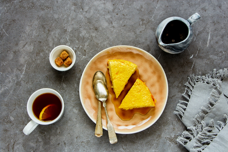 Breakfast with soft homemade cottage cheese cake, maple syrup and tea cup over grey background flat lay, top view.の写真素材