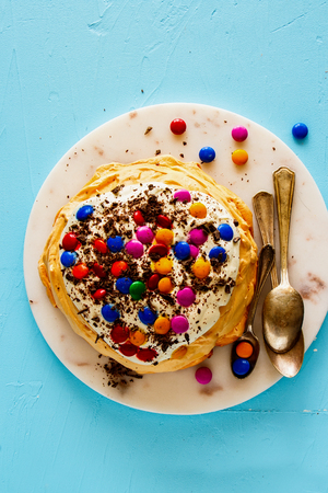 Flat-lay of Meringue Pavlova cake with colorful Sprinkles, whipped cream and chocolate on blue backgroundの写真素材