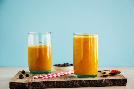 Healthy mango banana turmeric smoothie jars on blue backgroundの写真素材