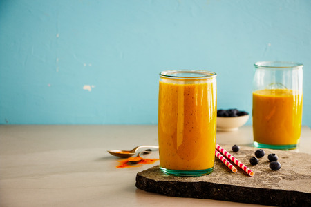 Fresh mango banana turmeric smoothie jars on blue backgroundの写真素材