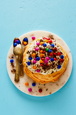 Flat lay of Pavlova cake with colorful Sprinkles, whipped cream and chocolate on blue backgroundの写真素材
