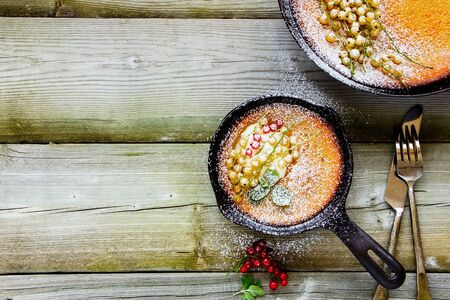 Homemade Danish pancake with red and white currant berries in frying pan, flat lay compositionの写真素材