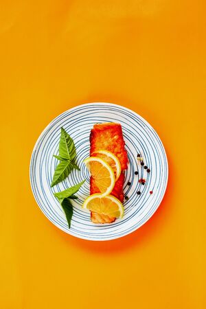 Grilled salmon with lemon and herbs on orange background, flat lay compositionの写真素材
