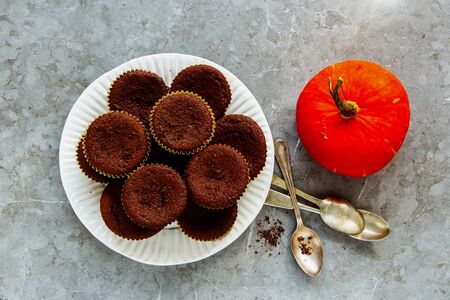Chocolate pumpkin cupcakes and orange pumpkin on grey concrete backgroundの写真素材