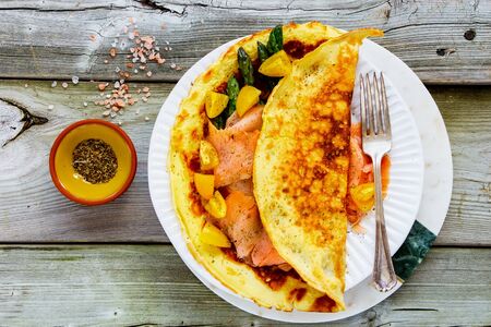 Flat-lay of omelette with smoked salmon and vegetables on wooden tableの写真素材