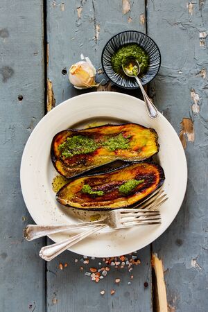 Flat-lay of roasted eggplant with pesto sauce on wooden board from above の写真素材