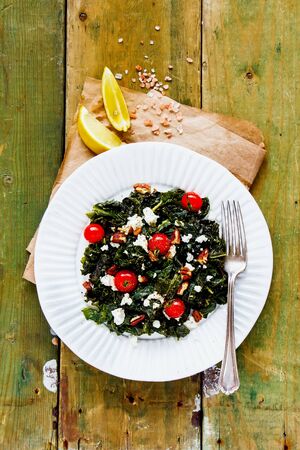 Fresh salad with kale, feta, nuts and tomato on wooden background flat layの写真素材